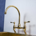 Unlacquered brass curved legs bridge faucet – installed over farmhouse sink